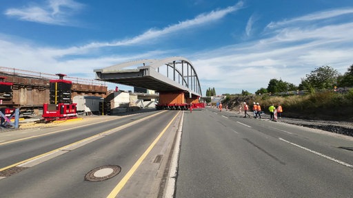 Eine fertige Brücke wird als ganzes Bauteil in eine Straßenführung eingesetzt.