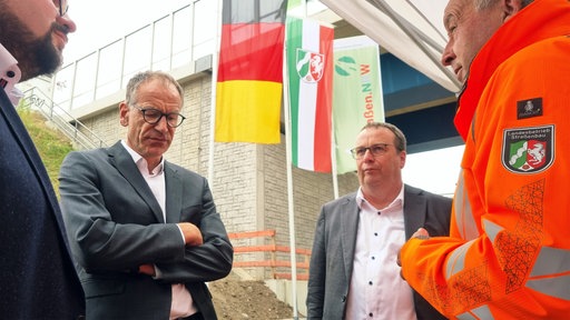 Mehrere Männer stehen neben einer Brücke im Kreis. Einer von ihnen ist NRW-Verkehrsminister Oliver Krischer