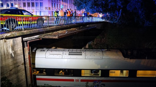 ein ICE steht unter einer Brücke auf der viele Einsatzkräfte stehen