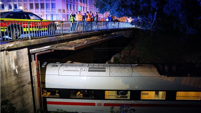 ein ICE steht unter einer Brücke auf der viele Einsatzkräfte stehen
