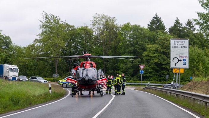 Rettungshubschrauber und Einsatzkräfte auf einer Straße. Zudem sind Fahrzeuge im Hintergrund.
