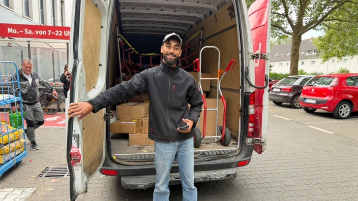 Paketzusteller Ali steht vor den geöffneten Türen seines Transporters