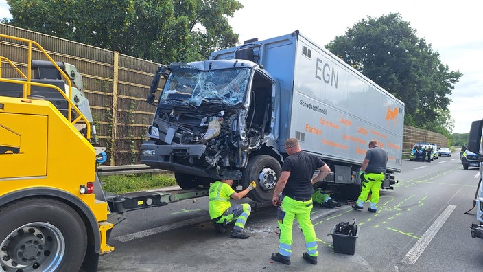 Ein beschädigter Lkw steht nach einem Unfall auf der Fahrbahn der A57, während mehrere Einsatzkräfte am Fahrzeug arbeiten.