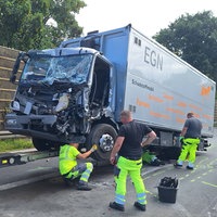 Ein beschädigter Lkw steht nach einem Unfall auf der Fahrbahn der A57, während mehrere Einsatzkräfte am Fahrzeug arbeiten.