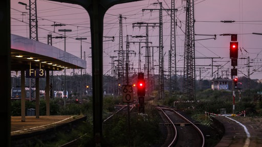 Man sieht eine Bahnstrecke mit rot leuchtenen Ampeln und einem lilanen Himmel.