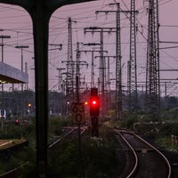 Man sieht eine Bahnstrecke mit rot leuchtenen Ampeln und einem lilanen Himmel.