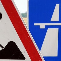 Ein Baustellenschild ist vor einem Autobahnschild platziert.