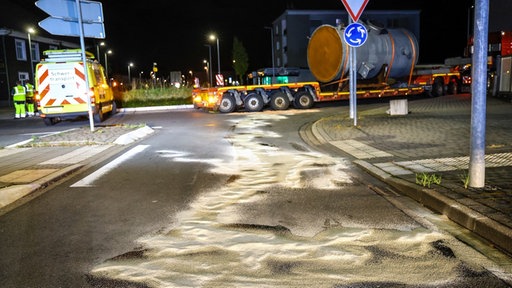 Ein Schwertransport steht mitten in einem Kreisverkehr, im Vordergrund erkennt man weißes Bindemittel auf der Fahrbahn.