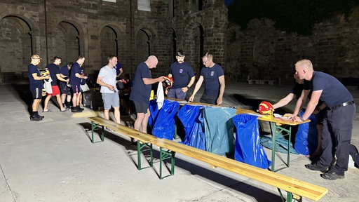 Im Innenhof eines ehemaligen Klosters stehen Bänke und Tische mit blauen Säcken, drumherum stehen Feuerwehrmann und räumen Gegenstände wie Helme in die Säcke