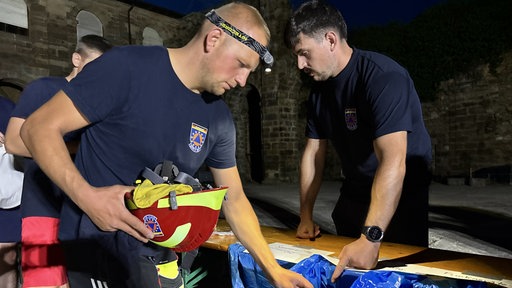 Ein Feuerwehrmann räumt seinen Helm in einen blauen Sack, im Hintergrund ist der Innenhof eines ehemaligen Klosters zu sehen