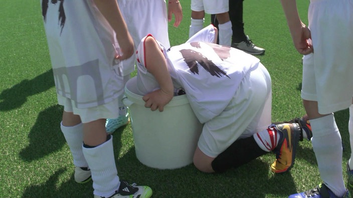 Nach einem Fußballspiel steckt ein Kind den Kopf in einen Eimer mit Wasser