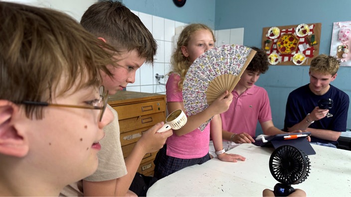 Schüler kühlen sich mit Fächern und Ventilatoren ab.