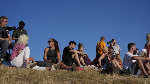 Einige Menschen sitzen zusammen auf einer Wiese und warten auf die Sonnenfinsternis