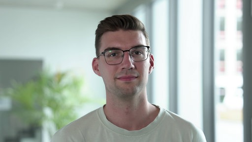 Ein junger Mann mit Brille blickt in die Kamera