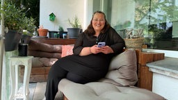 Eine Frau sitzt mit ihrem Handy in der Hand auf einem Balkon 