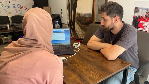 Der Sozialberater Malek Khaled sitzt mit einer Klientin am Schreibtisch und schaut auf einen Laptop.