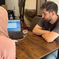 Der Sozialberater Malek Khaled sitzt mit einer Klientin am Schreibtisch und schaut auf einen Laptop.