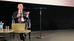 Bert Woudstra sitzt vor der Kinoleinwand und spricht in ein Mikrofon.
