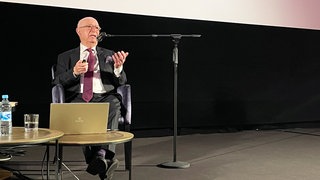 Bert Woudstra sitzt vor der Kinoleinwand und spricht in ein Mikrofon.