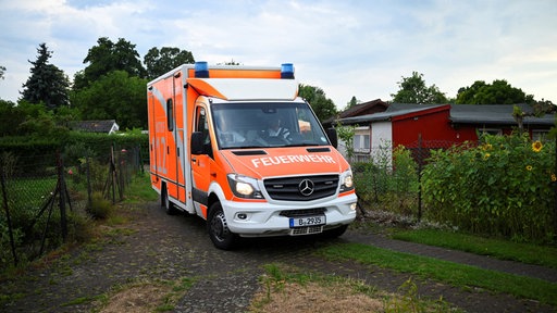 Ein Rettungswagen der Feuerwehr Berlin steht auf einem Weg einer Kleingartenanlage.
