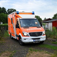 Ein Rettungswagen der Feuerwehr Berlin steht auf einem Weg einer Kleingartenanlage.