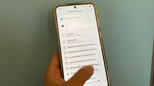 Eine Hand hält ein Handy, zu sehen ist die App rufmobil.nrw 