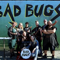 Die Inszenierung Bad Bugs des Theater Marabu in Bonn. Die Schauspieler posieren auf der Bühne. Im Hintergrund steht Bad Bugs auf der Wand. Man sieht Musikinstrumente.