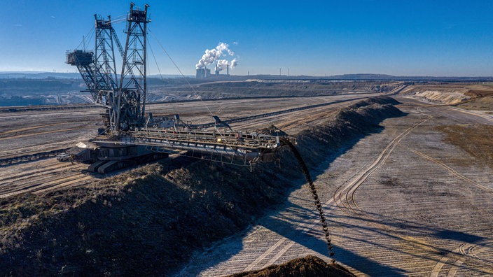 Inden-Viehöven, 08.02.2023. Bagger im RWE Tagebau Inden befördert Abraum von einem Förderband auf eine Halde. Kohlekraftwerk Weisweiler im Hintergrund.