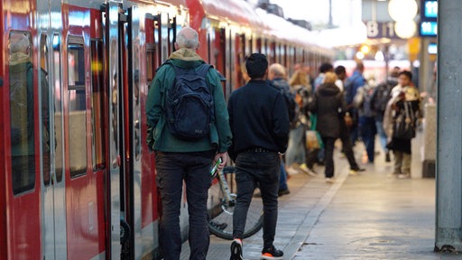 Eine rote S-Bahn steht an einem Bahnsteig. Menschen steigen ein und aus.