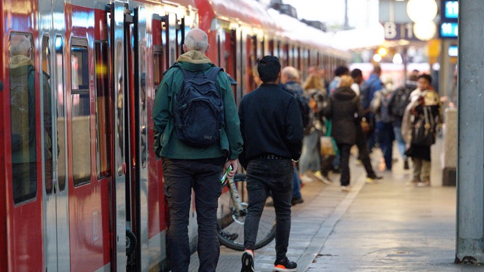Eine rote S-Bahn steht an einem Bahnsteig. Menschen steigen ein und aus.