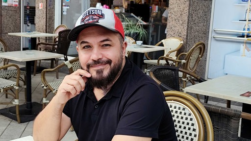 Ein südländisch aussehender Mann mit Kappe und schwarzem Poloshirt.
