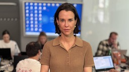 Kriminaldirektorin Jessica Bouška guckt geradeaus in die Kamera. Hinter ihr sitzen Menschen an einem Schreibtisch an Laptops.