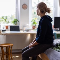 Weibliche Jugendliche sitzt alleine auf dem Bett und schaut zum Fenster