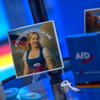 Sticker stehen auf einem Glastisch mit dem Slogan Generation deutschland. Auf dem einen ist eine blonde Frau in einem Dirndl zu sehen. Alle hhaben das AfD Logo drauf.
