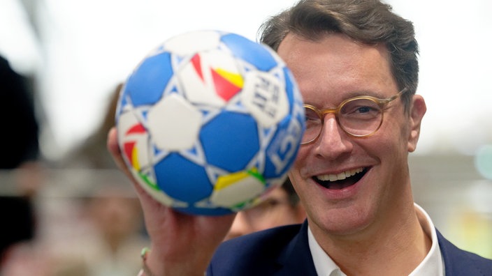 Hendrik Wüst (CDU) hält einen Handball in die Kamera