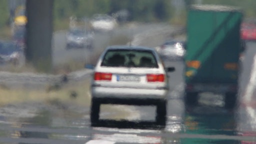 Flimmernde Straße im Sommer, ein verschwommenes graues Auto fährt.