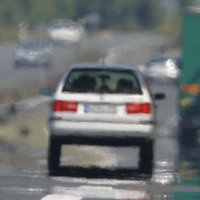 Flimmernde Straße im Sommer, ein verschwommenes graues Auto fährt.