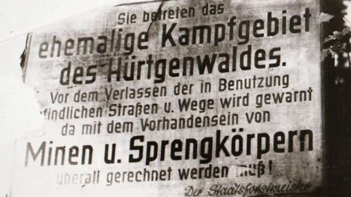 Schild im Hürtgenwald: " Sie betreten das ehemalige Kampfgebiet des Hürtgenwaldes. Vor dem Verlassen der in Benutzung befindlichen Straßen u. Wege wird gewarnt da mit dem Vorhandensein von Minen u. Sprengkörpern überall gerechnet werden muß!"