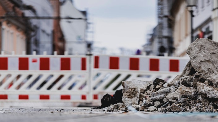Ein Bauzauhn steht auf einer Straße. Davor liegt Bauschutt.