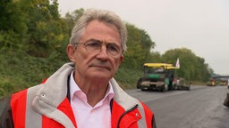 Peter Hübner, Vorstandmitglied Strabag, in einer orangenen Warnweste an einer Straße, die neu asphaltiert wird mit Baumaschine im Hintergrund.