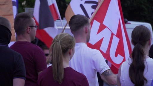 Man sieht junge Menschen auf einer rechtsextremen Demo von hinten. Im Hintergrund ist die Flagge der Jugendorganisation Junge Nationalisten zu sehen. 