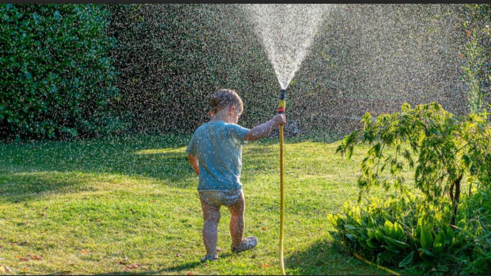 Kind im Garten mit Wasserschlauch
