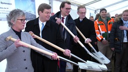 Verantwortliche, unter anderem der damalige NRW Verkehrsminister Hendrik Wüst (CDU), posieren mit Spaten für ein Foto beim symbolischen Spatenstich zum Neubau der Leverkusener Rheinbrücke