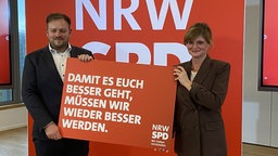 Sarah Philipp und Frederick Cordes bei einem Pressetermin mit einem Schild zur Kampagne "Wir haben verstanden."