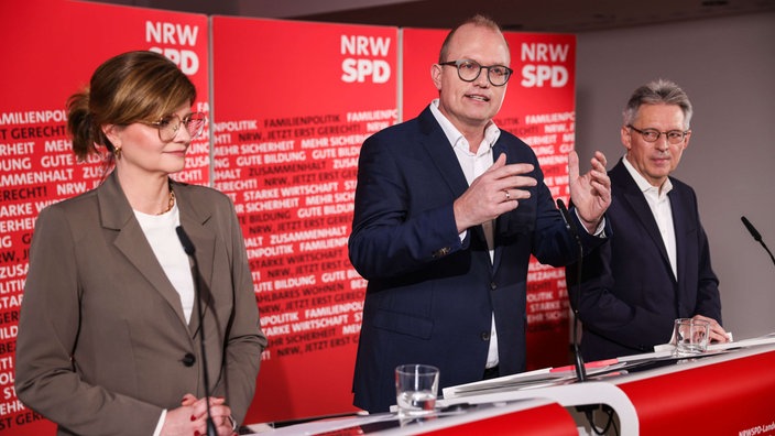 Sarah Philipp, Jochen Ott und Achim Post (von links nach rechts) stehen vor einer roten Wand mit SPD-Logo und geben eine Pressefkonferenz