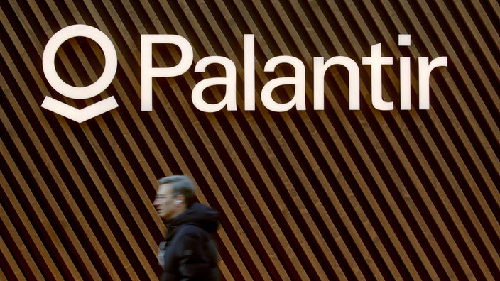Name und Logo des Softwareunternehmens Palantir an einer Wand, im Vordergrund läuft ein Mensch vorbei