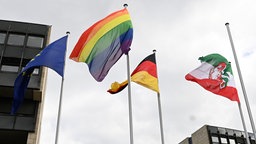 Vor dem Landtag in Düsseldorf weht eine Regenbogenflagge neben einer Deutschlandflagge, einer Europaflagge und einer Flagge mit dem NRW-Landeswappen.