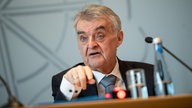 Herbert Reul, NRW- Innenminister, spricht an einem Tisch sitzend in ein Mikrofon einer Pressekonferenz.