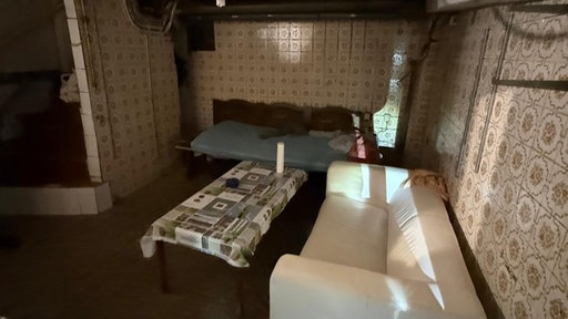 Bewohnte Unterkunft in einer Schrottimmobilie in Hagen - im Bild eine Couch und ein Tisch in einer verwahrlosten Wohnung