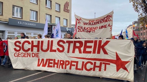Mehrere Menschen laufen eine Straße entlang und halten ein Banner hoch auf dem steht "Schulstreik gegen die Wehrpflicht"
